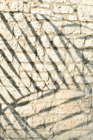 A close-up vertical shot of an old, rough stone wall, featuring striking diagonal shadows creating an abstract pattern. This textured background offers ample copy space for graphic design projects.の写真素材