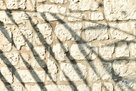 A close-up horizontal shot of an old, rough stone wall, featuring striking diagonal shadows creating an abstract pattern. This textured background offers ample copy space for graphic design projects.の写真素材