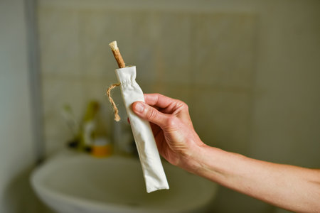 Close-up of a senior womans hands holding and removing a natural miswak toothbrush stick from a reusable cotton bag over a bathroom sink. Zero waste sustainable oral hygiene concept.の写真素材