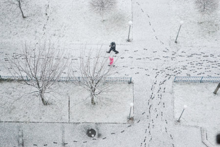 An aerial view of a snowy pedestrian street in Kyiv, Ukraine, with two people walking and many footprints visible in the fresh white snow. Represents winter weather, urban life, and travel. Horizontalの写真素材
