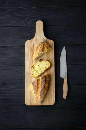 Bread on a wooden board with a knife on a black background