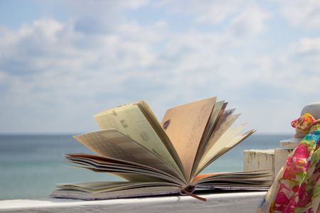 Book and scarf in the beach on background sky. Romance in the sea
