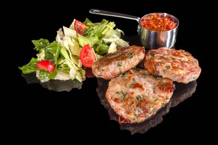 Delicious lamb meatballs served with fresh salad and mashed tomatoes with reflection, isolated on black backgroundの写真素材