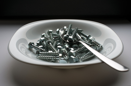 White plate and spoon filled with stainless steel screws