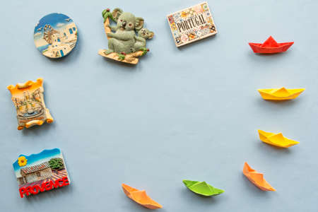 colorful paper ships and  various souvenir magnets from several world country arranged on the blue backgroundの写真素材