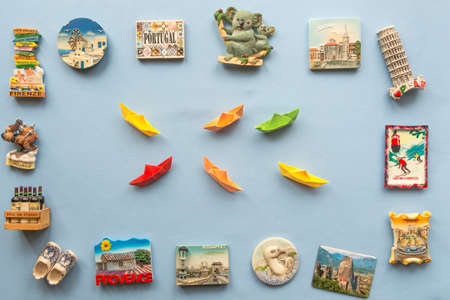colorful paper ships and  various souvenir magnets from several world country arranged on the blue backgroundの写真素材