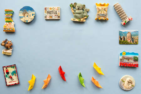 colorful paper ships and  various souvenir magnets from several world country arranged on the blue backgroundの写真素材