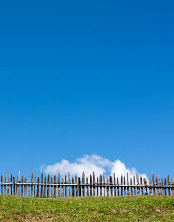 Green grass field with wooden fence against blue skyの写真素材