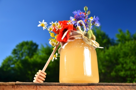 jar full of delicious fresh honey honey dipper and wild flowers in apiary against blue skyの写真素材