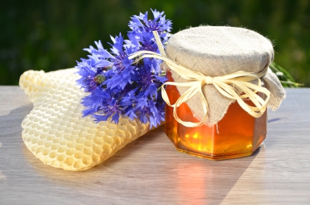 jar full of delicious fresh honey piece of honeycomb and wild flowers in apiaryの写真素材
