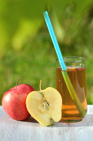 glass of delicious apple juice and apple on table in gardenの写真素材