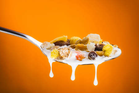 Delicious fruity muesli on spoon with milk on gradient orange background