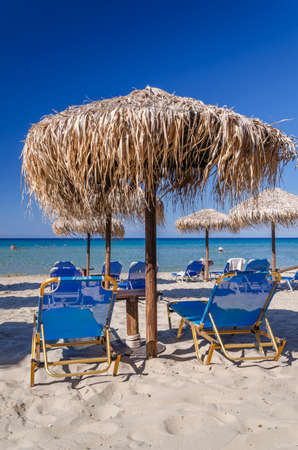 Straw beach umbrellas and sun chairs on a sandy beach on the east coast of Zakynthos island in Greeceの写真素材