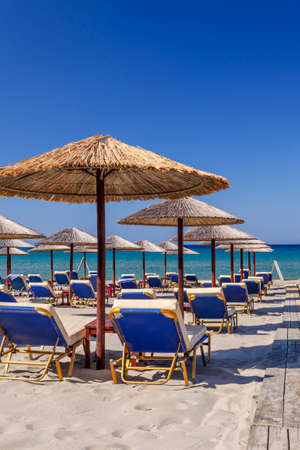 Straw beach umbrellas and sun chairs on a sandy beach on the east coast of Zakynthos island in Greeceの写真素材