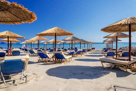 Straw beach umbrellas and sun chairs on a sandy beach on the east coast of Zakynthos island in Greeceの写真素材