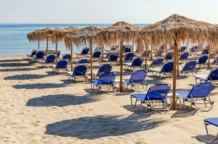 Straw beach umbrellas and sun chairs on a sandy beach on the east coast of Zakynthos island in Greeceの写真素材