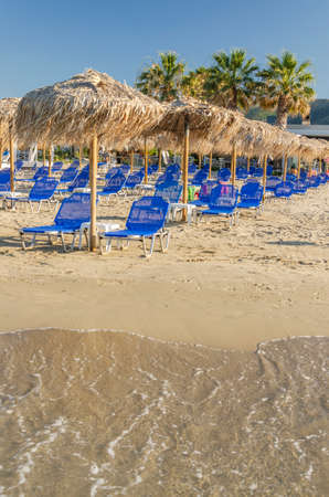 Straw beach umbrellas and sun chairs on a sandy beach on the east coast of Zakynthos island in Greeceの写真素材