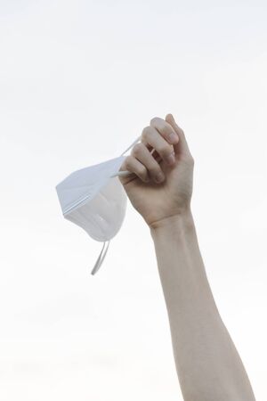 Arm holding a face mask in the air on a blue background in nature in a isolated backgroundの写真素材