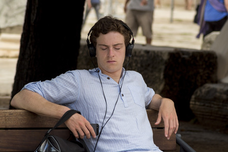 ZADAR, CROATIA - AUGUST 17, 2015: Young tourist resting on bench, listening music through headphones in Dalmatian town of Zadarのeditorial素材