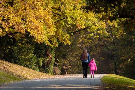 Mother and daughter walk through park in autumnの写真素材