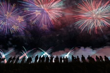 Group of people enjoying fireworks show in a carnival or holiday. People in silhouette and blurred American flag in background.の写真素材