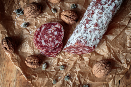 Italian salami with walnuts on craft paper on rustic  wooden backgroundの写真素材