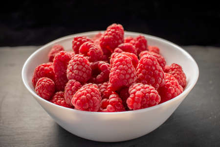 Raspberries in white bowl on black stone backgroundの写真素材