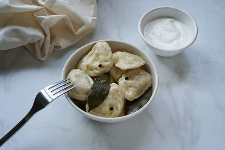 Dumplings in a beige ceramic bowl with sour cream on a light surface.