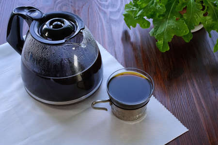 Glass coffee pot and vintage glass in a silver cup holder filled with black coffee. Wooden surface. Morning coffeeの写真素材