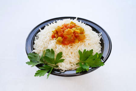 White basmati rice with stewed zucchini, tomato and other vegetables on top and served on a black ceramic plate. High angle. Light backgroundの写真素材