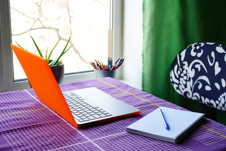 Laptop and notepad on the table by the window at home. Remote place of work or online study.の写真素材