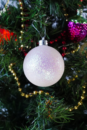 White shiny ball hanging on a Christmas tree, vertical photo. Close-up of a Christmas tree decorated with baubles. Template, background for greetings, greeting card.の写真素材