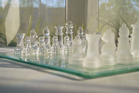 Glass chess on a white table in a bright, sunny room. Space for text. The concept of hobby and leisure. Eye level view.の写真素材