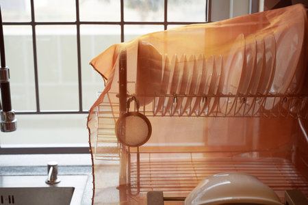 Clean dishes are neatly arranged on a drying rack and covered with a transparent cloth to protect...
