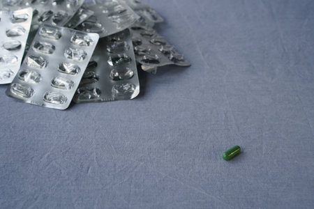 A single green capsule lies separately from a pile of empty blister packs on a plain background with...