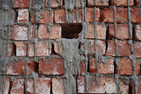 Untidy brickwork with gaps between uneven chopped bricks unfilled with cement mortar. Gray cement...