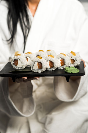 Sushi rolls on a black plate in the hands of a girl in a white robeの写真素材
