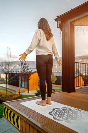 Young woman standing on terrace of house and looking at sunset.