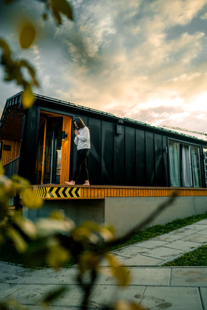 Young man standing in front of a modern house and looking at the sunsetの写真素材