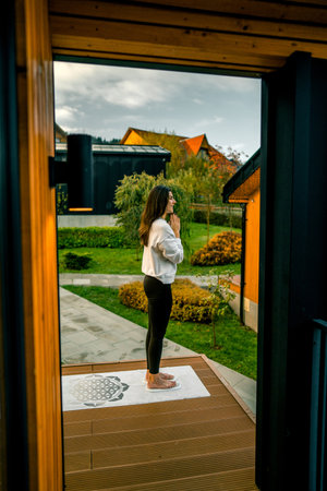 A young woman in a white shirt and black pants is standing on the terrace of her house.の写真素材