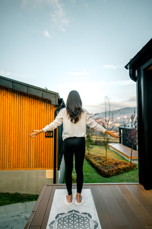 Young woman stands on nails on the terrace near the house early in the morning.