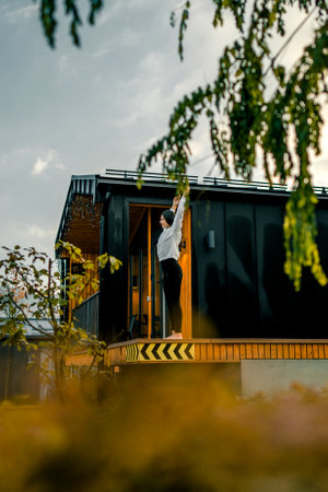 Young woman standing on the terrace of her modern house. Sunset.の写真素材