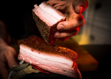 Close-up of the hands of a professional chef in a black apron preparing a sandwich with bacon and spicesの写真素材