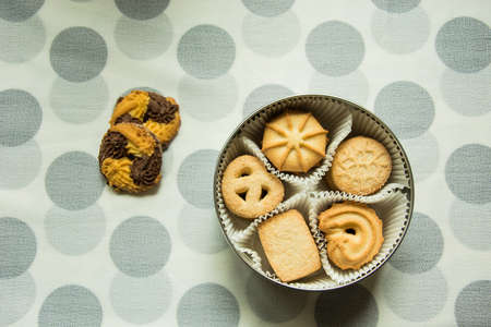 Cookies with sugar in a round box and two lying on a tablecloth with polka dots