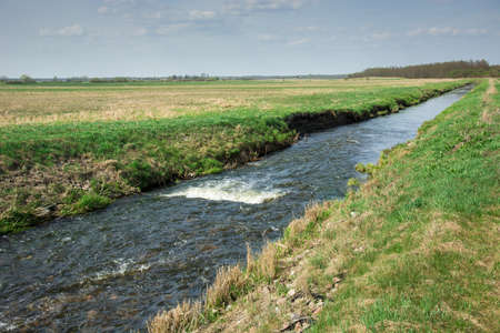 Wild river Uherka flowing through fields in eastern Poland and blue sky - view on a spring sunny day