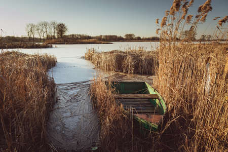 A green boat hidden in the reeds on a frozen lakeの写真素材