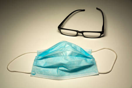 Surgical blue mask and black glasses lying on a white