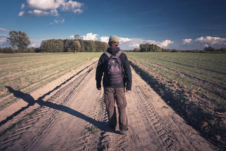Traveler with backpack walking the dirt road, view in sunny dayの写真素材