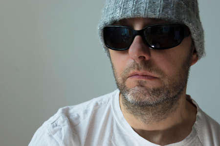 Portrait of a single man in sunglasses, a winter hat and a white T-shirtの写真素材