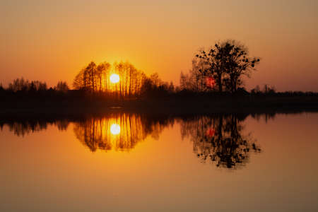 The reflection in the water of the sunset behind the trees, spring evening viewの写真素材